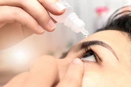 A person putting eye drops in their eye